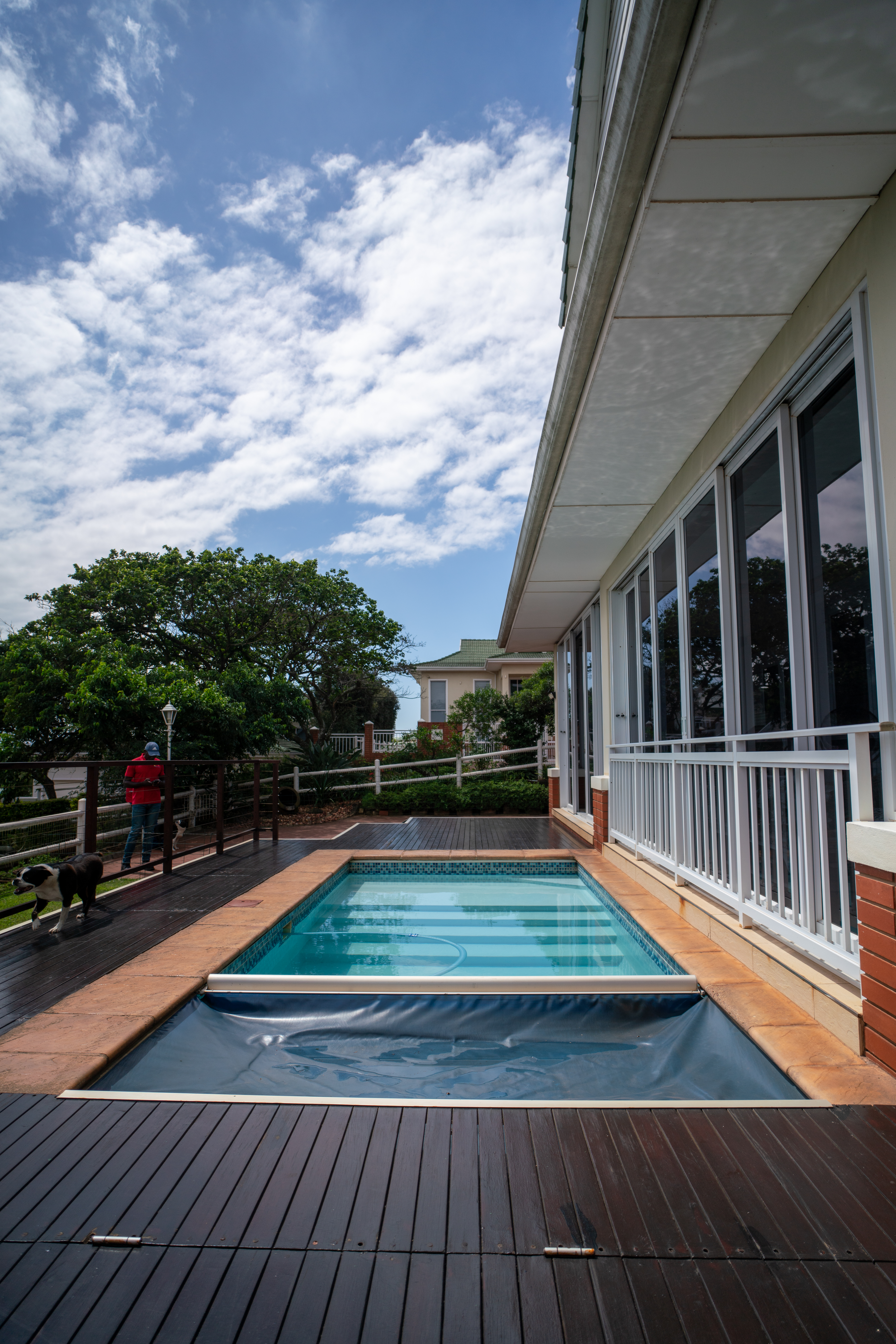 Automatic vinyl pool cover partially open showing secure track system and wooden pool deck